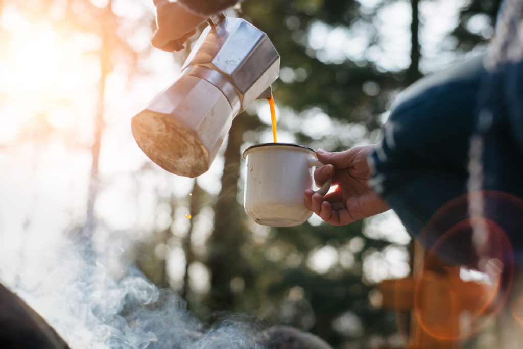 woman pours hot coffee in mountains near campfire