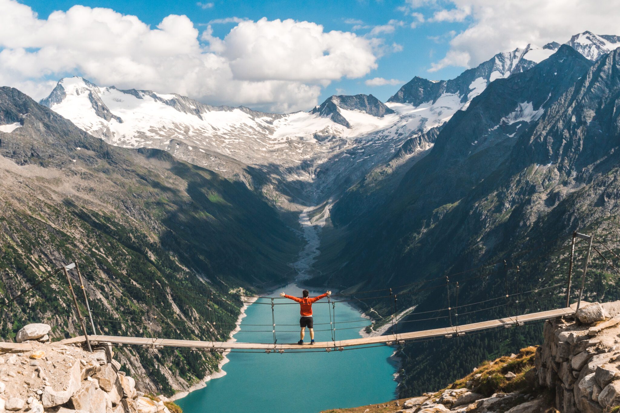 Man in a red tshirtjacket sitting on a suspension bridge above the Alps. Freedom and adventure concept. Touristic activities in Austrian Alps.