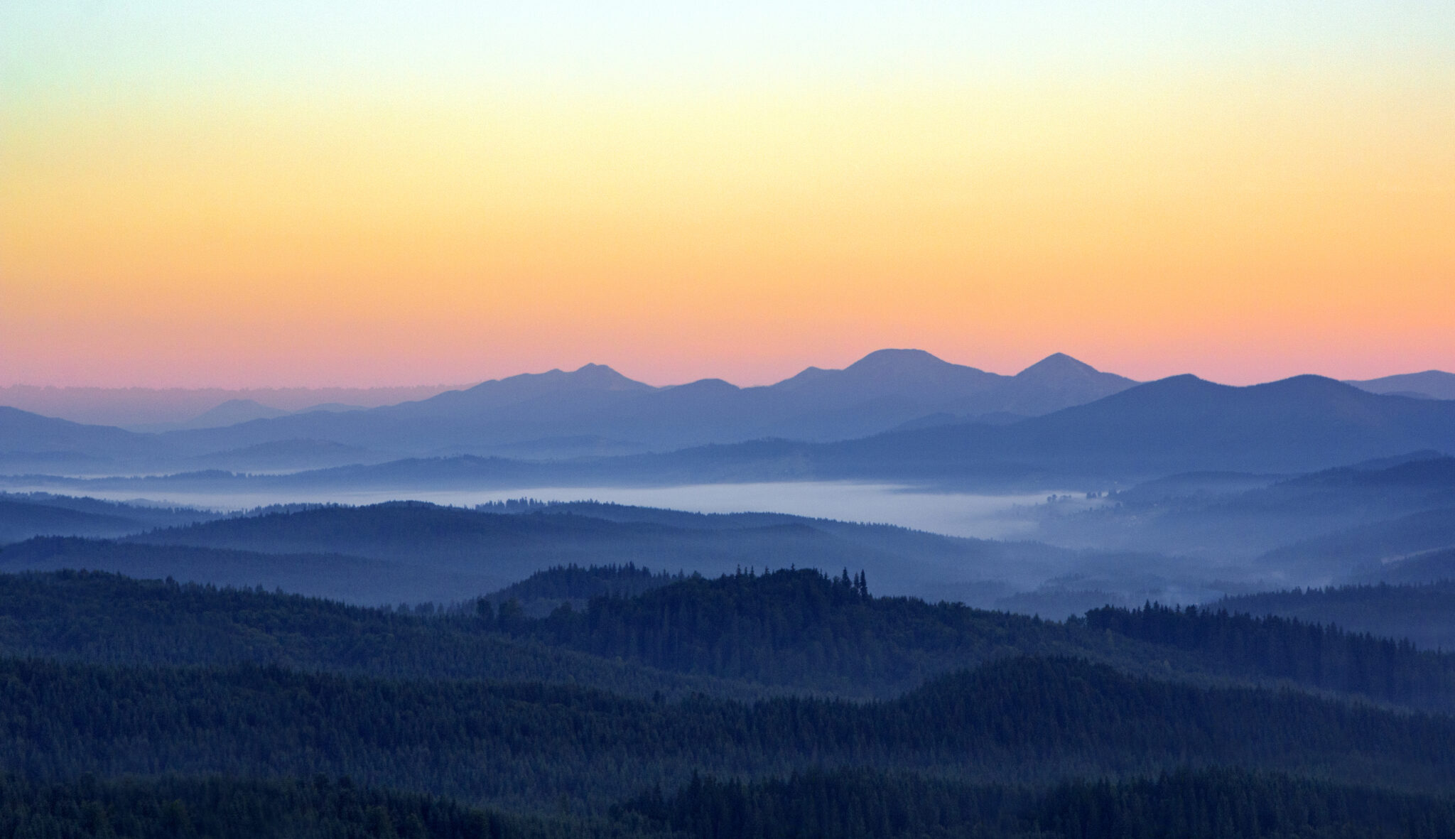 Foggy morning in the mountains with silhouettes of hills. Serenity sunrise with soft sunlight and layers of haze. Mountain landscape with mist in woodland in pastel colors