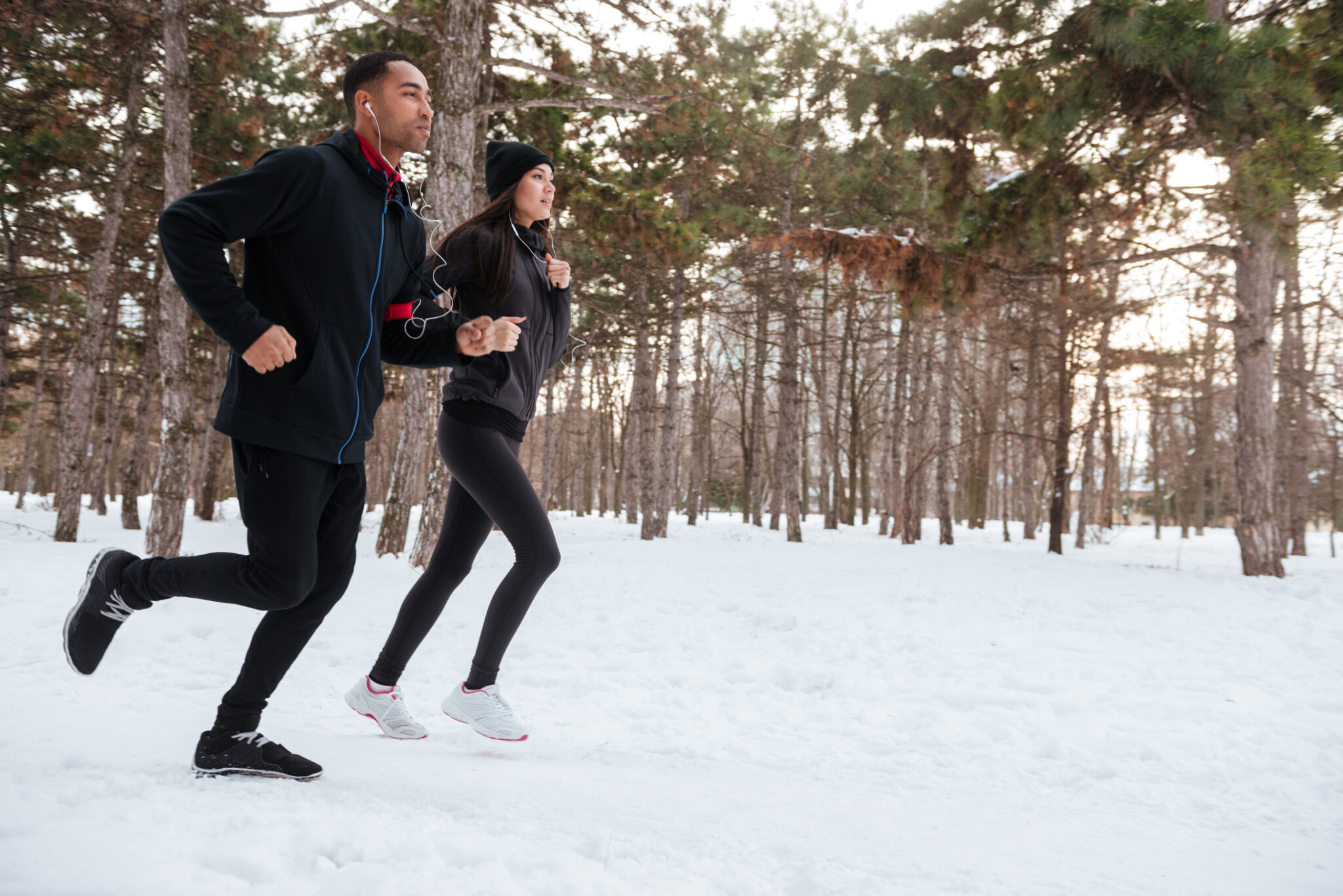 Side view of a young fitness couple running in the forest in winter