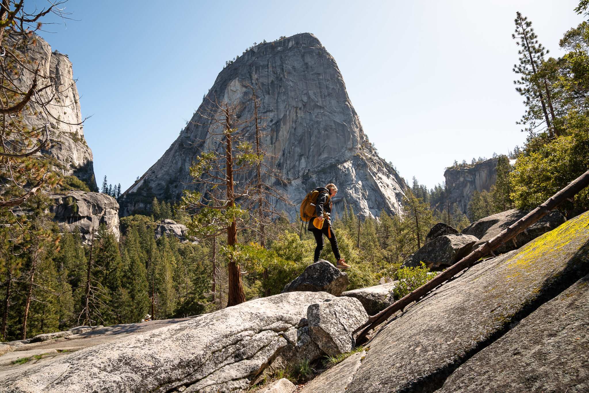 Woman hiker with a yellow backpack on her back climbing a stone path below Half Dome and Nevada and Vernal Fall in Yosemite National Park