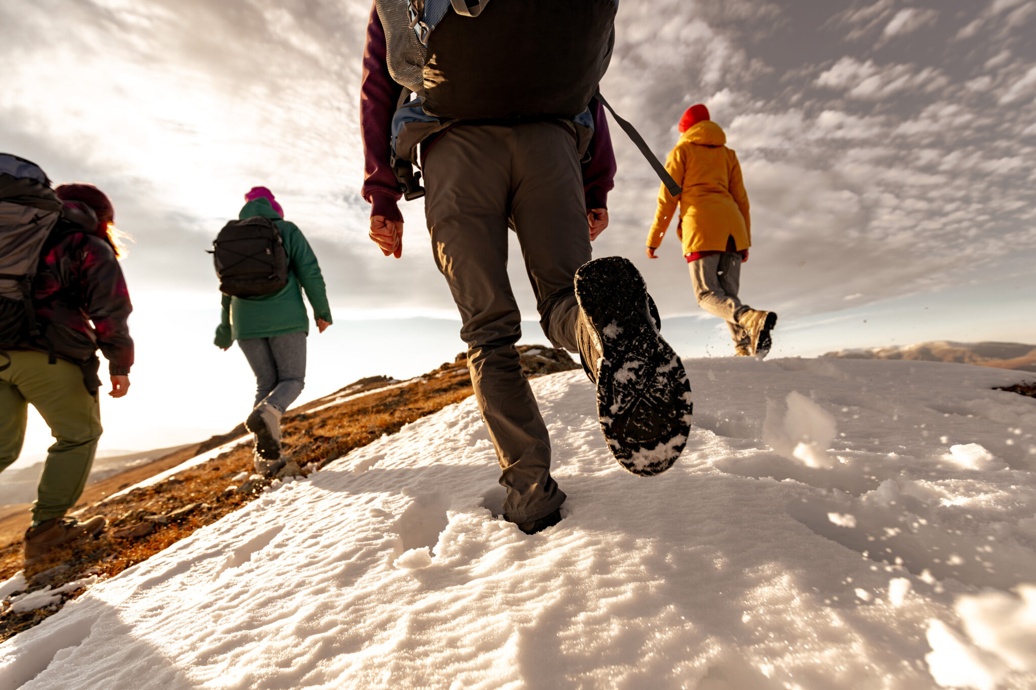 Group of sporty young tourists with backpacks walks at mountain top. Close up photo of hikers legs and silhouettes