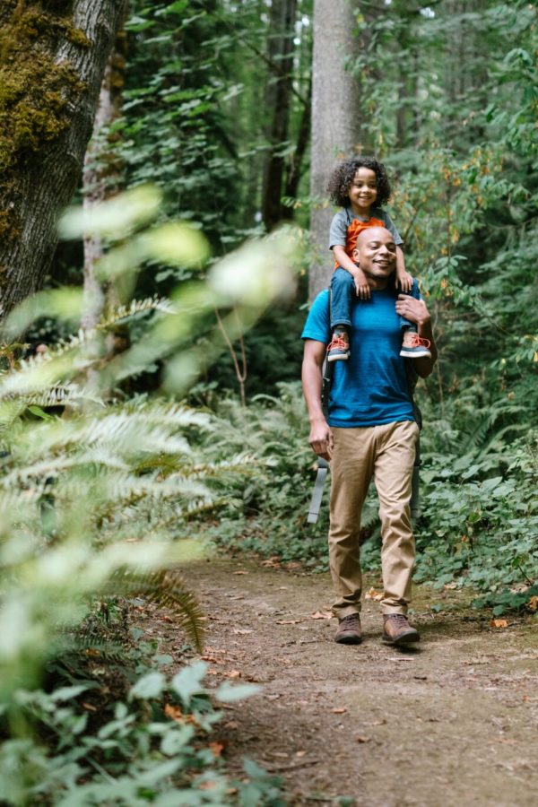 A young mixed race family spends time together outside in Washington state, enjoying the beauty of the woods in the PNW.  The dad holds his boy on his shoulders.